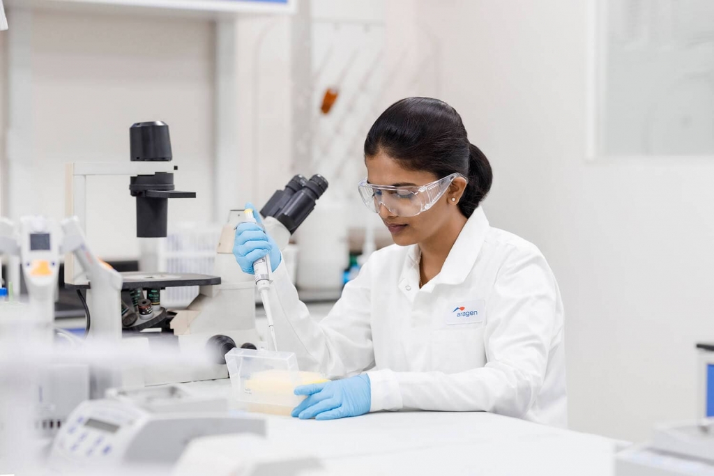 Aragen scientist in safety glasses pipetting at a laboratory bench, representing small molecule services