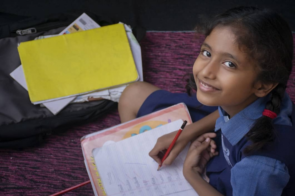 Smiling schoolgirl writing in a notebook, representing Aragen's corporate social responsibility programmes