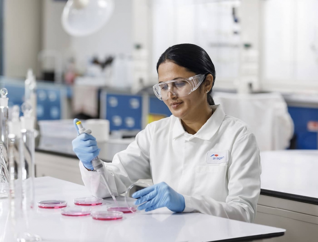 Aragen scientist in safety glasses pipetting into petri dishes at a quality control bench